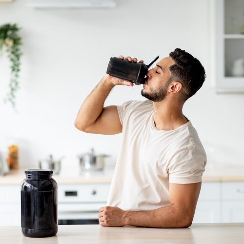 Young Arab guy drinking protein shake from bottle at kitchen, copy space. Millennial Eastern man using meal replacement for weight loss, having sports supplement for muscle gain. Body care concept